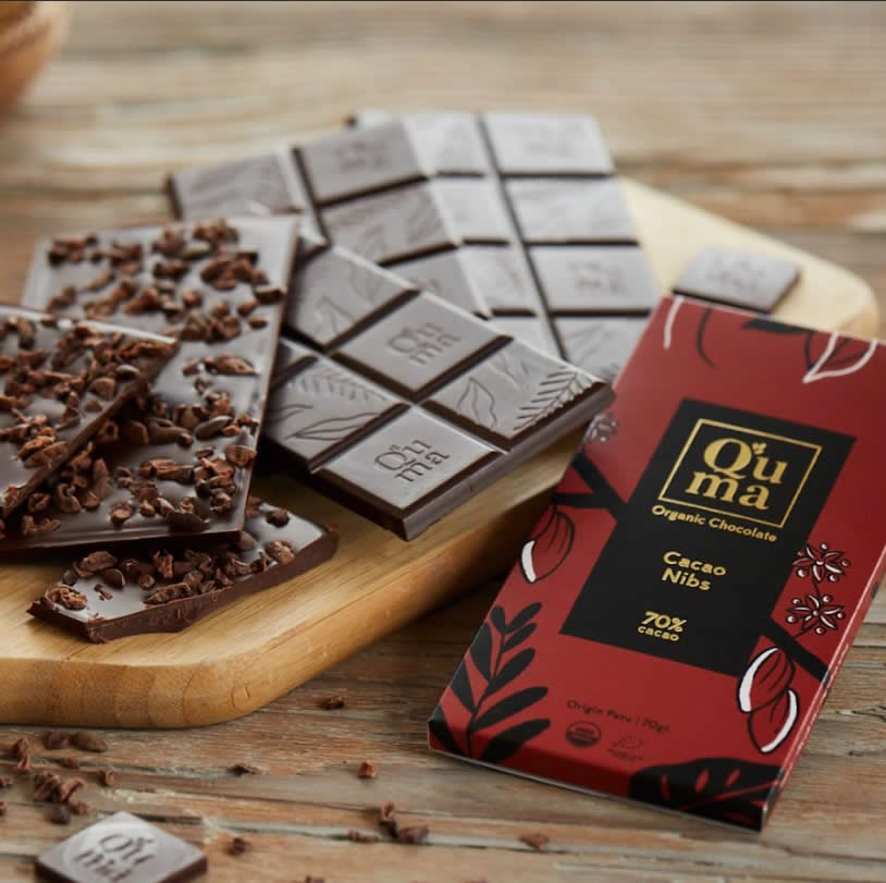 Q'uma cacao nibs bar broken on a wooden board with loose nibs