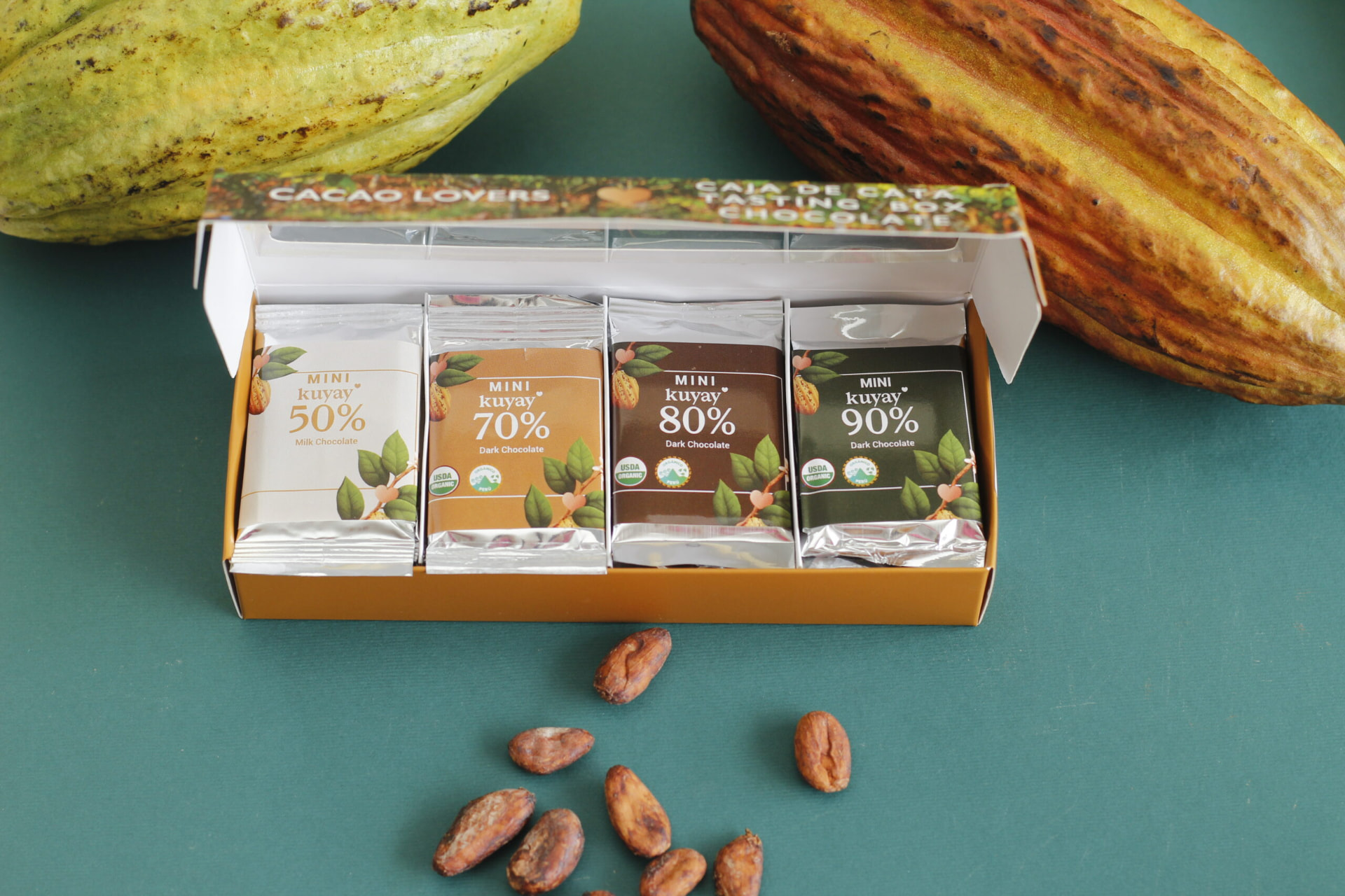 Kuyay Caja de Cata open with 50%, 70%, 80% and 90% mini bars beside cacao pods