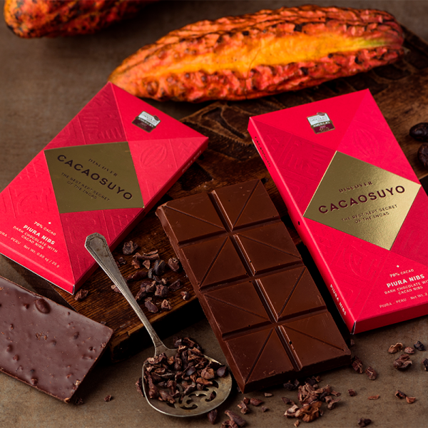Two Cacaosuyo Piura Nibs bars beside a cacao pod and a spoon of cacao nibs